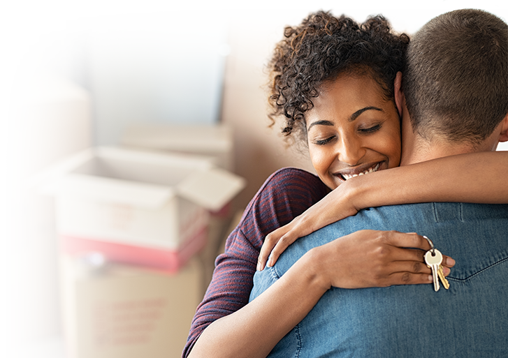 Photo of a woman hugging a person with a set of keys in her hands and unpacked boxes in the background. Photo of a woman hugging a person with a set of keys in her hands and unpacked boxes in the background.