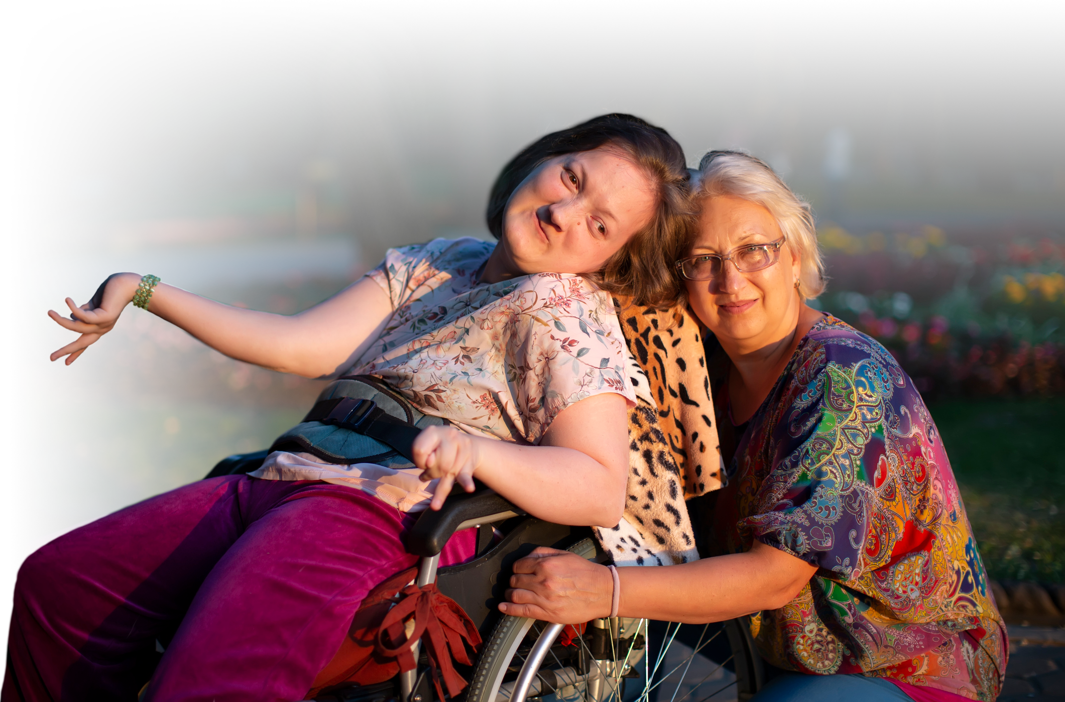 Photo of an adult daughter powerchair-user with her mother, both smiling at the camera.